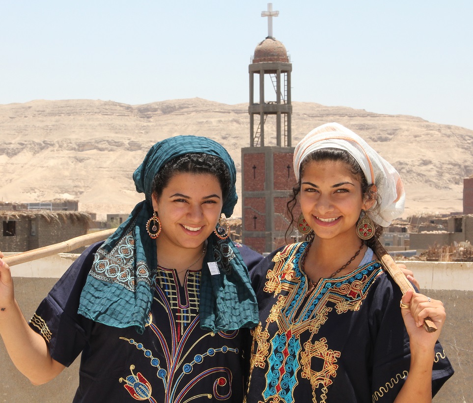 Two young women wearing galabeyas stand in front of a Coptic church in Egypt.